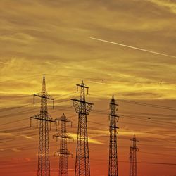 Low angle view of electricity pylon against sky during sunset