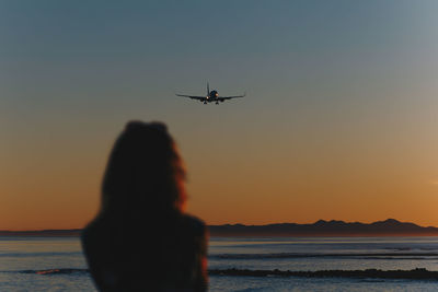 Rear view of woman standing at beach against sky during sunset