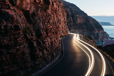 Light trails on road amidst rock formation against sky