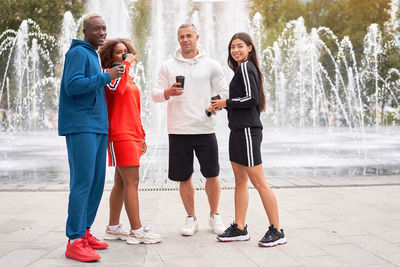 Full length portrait of friends holding coffee cup standing against fountain