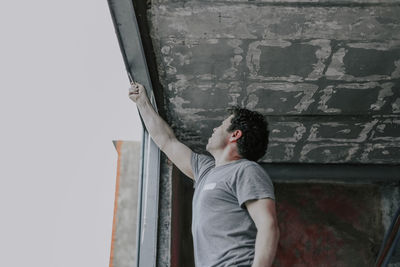 A young caucasian man cleans the garbage with a construction knife from a window opening