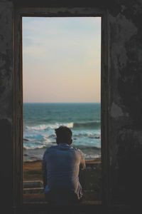 Rear view of man sitting at beach against sky