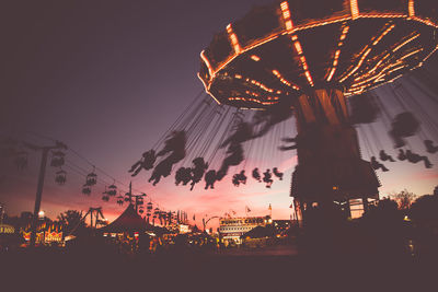 Low angle view of chain swing ride at sunset