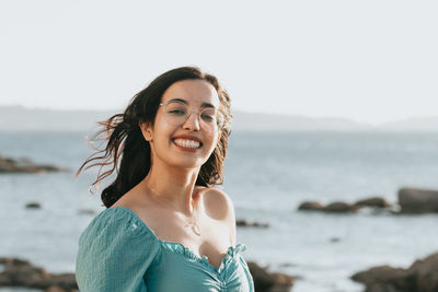 Portrait of smiling young woman at beach against sky