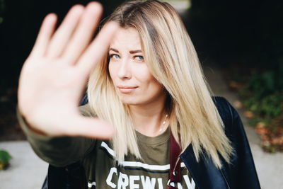 Portrait of young woman showing stop gesture while standing outdoors