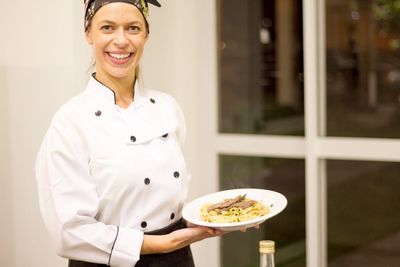 Portrait of happy female chef holding pasta in plate while standing in commercial kitchen
