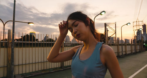 Young woman standing by railing against sky in city