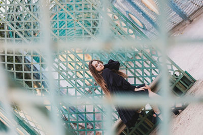 Side view of woman looking through chainlink fence