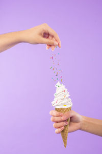 Cropped hands sprinkling sprinkles on ice cream against purple background