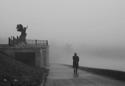 Man walking on footpath by statue in foggy weather