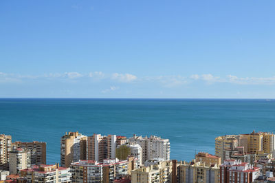 Buildings by sea against blue sky