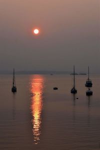 Silhouette sailboats moored on sea against sky during sunset