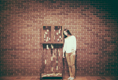 Young woman standing against brick wall