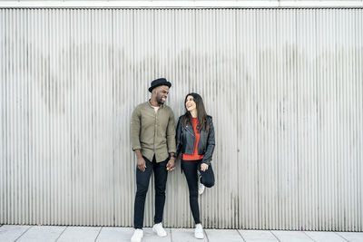 Full length of laughing couple standing against wall