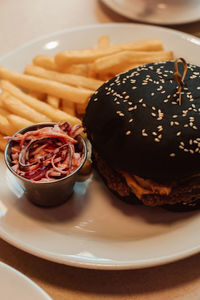 French fries and a beef burger with a black bun in a cafe. american delicious lunch