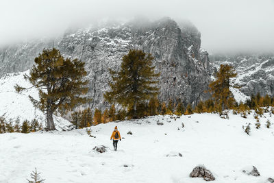 Rear view of female hiker walking on snowy path under amazing misty mountains