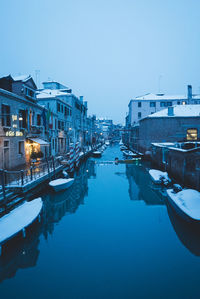 Canal in city against clear blue sky