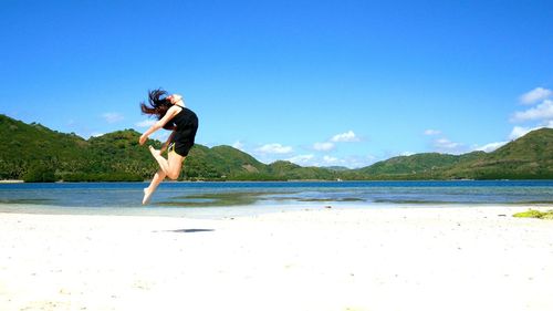 Full length of young woman jumping at beach against sky