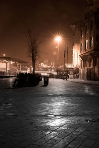 Illuminated street by buildings against sky at night