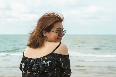 Beautiful young woman looking at sea against sky