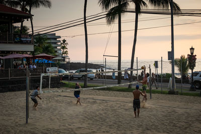 People playing on beach against sky during sunset