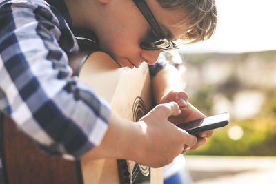 Boy using smart phone while leaning on guitar