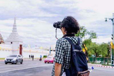 Rear view of man photographing against sky in city