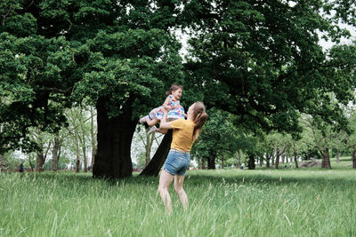 Mother lifting daughter while standing on grass in park