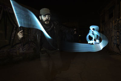 Digital composite image of mature man with light painting on street amidst graffiti wall