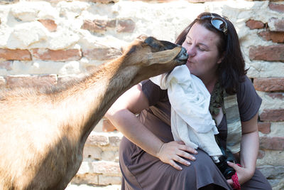 Woman kissing goat against wall