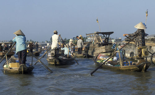 Vendor oaring boat in river against clear sky