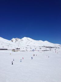 People skiing on snowcapped mountain against clear sky