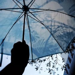 Low angle view of hand holding umbrella against sky