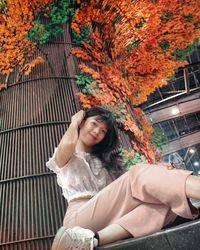 Portrait of smiling young woman sitting against building in city