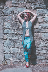 Young woman wearing sunglasses standing against wall