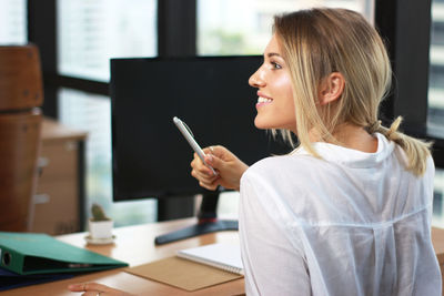 Rear view of businesswoman smiling while sitting at desk in office