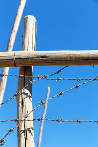 Low angle view of barbed wire fence against clear blue sky