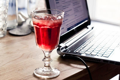 Close-up of red drink in glass by laptop on table 