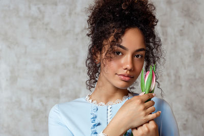 Portrait of smiling young woman holding tulip while standing against wall