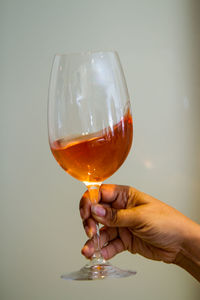 Cropped hand of person holding alcoholic drink against wall