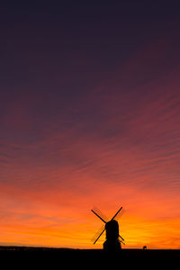 Silhouette of traditional windmill against orange sky