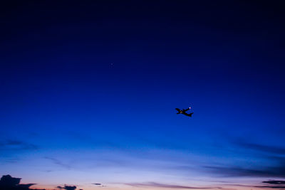 Low angle view of silhouette airplane against blue sky