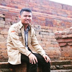 Portrait of young man sitting against brick wall