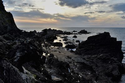 Rock formation on beach against sky during sunset