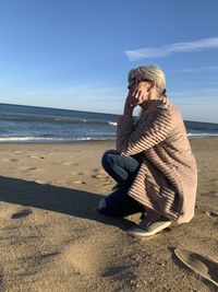 Woman sitting on sand at beach against sky