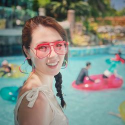 Preety smiling asian lady colorful glasses earringa swimming pool inflatables blue green summer