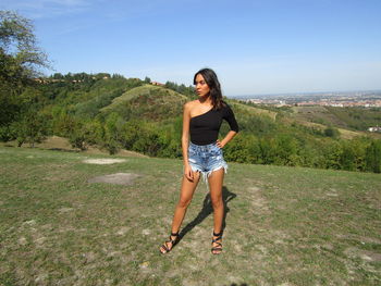 Full length portrait of young woman standing on land against sky