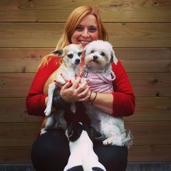 Portrait of young woman with dogs sitting against wooden wall