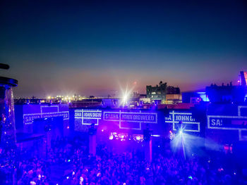 Crowd at illuminated city against clear blue sky at night