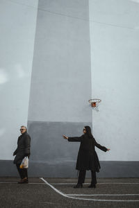 Rear view of woman with arms outstretched standing against wall